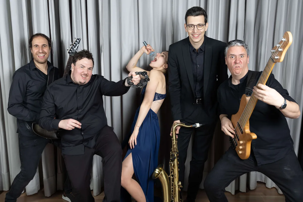 Die fünf Musikerinnen und Musiker von Iris' Coffeeshop in ausgelassener Pose mit Saxophon, Bass, Gitarre und Tamburin